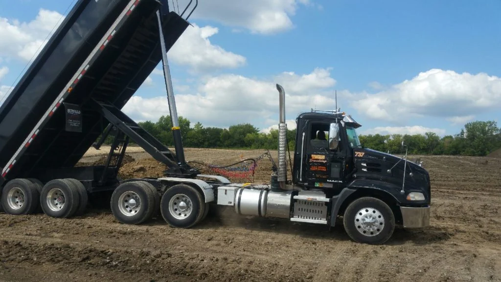 Black Trim's Trucking dump truck unloading at a work site